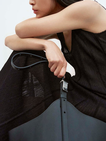 Cropped image of model wearing Tavia Dress in Viscose Fringe Knit in black, carrying Brant Bag in black holding the Brant Bucket Bag in Smooth Calf