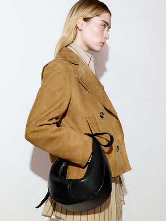 Cropped image of the side of a model standing against a white backdrop in the Addy Top in Stripe Cotton Silk in Taupe, Nola Jacket in Suede in Pony, carrying the Mini Slide Bag in Black