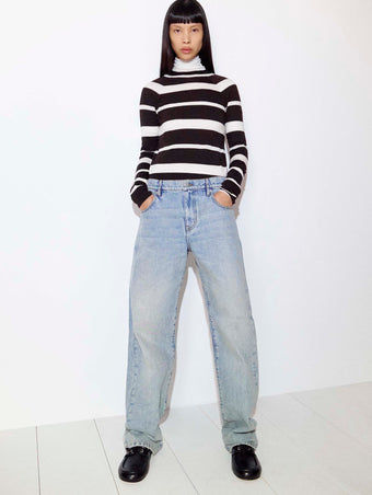 Cropped image of model standing against a white wall in the Gia Top in Superfine Merino Silk in Brown Multi, the Sherman Jean in Light Wash, and the Deck Shoes in Nappa in Black