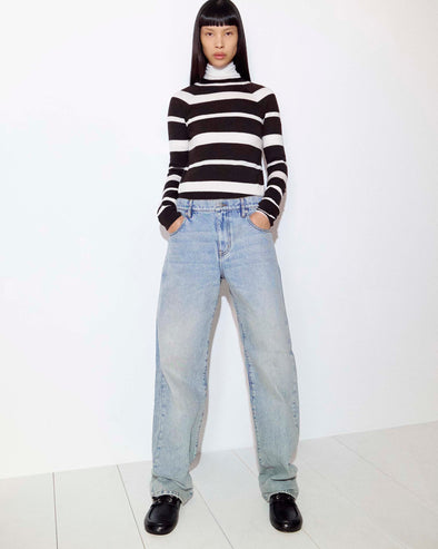 Cropped image of model standing against a white wall in the Gia Top in Superfine Merino Silk in Brown Multi, the Sherman Jean in Light Wash, and the Deck Shoes in Nappa in Black
