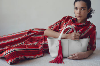 Image of model Elise Kouzou wearing red striped set holding the white East West tote laying on a white carpet against a white wall 