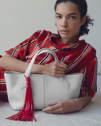 4x5 cropped image of model Elise Kouzou laying on white carpet holding the East West Chelsea tote 