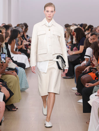 Model Walking Proenza Schouler SS24 Runway In Roos Jacket In Ecru Lacquered Leather, Adele Skirt In Ecru Lacquered Leather, City Messenger Bag In Natural Canvas, Soft Square Slippers In Cream Canvas