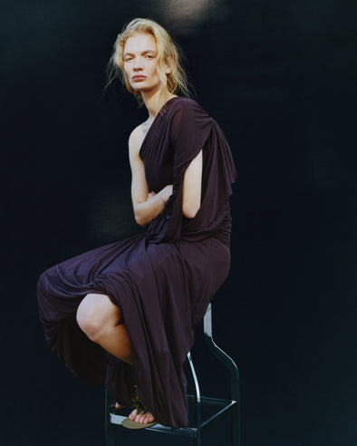 Proenza Schouler image of model sitting on a stool wearing Gabri Dress in Gauzy Pleated Jersey in Aubergine
