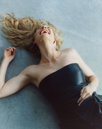 Proenza Schouler Image of Woman wearing Black Alonna Dress in Leather Laughing on a grey background
