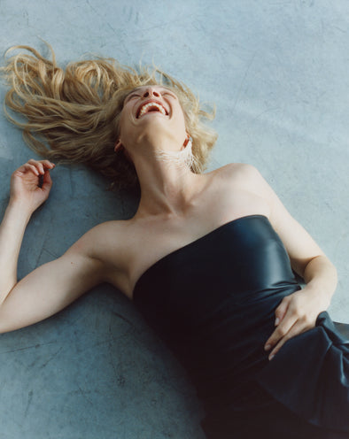 Proenza Schouler Image of Woman wearing Black Alonna Dress in Leather Laughing on a grey background