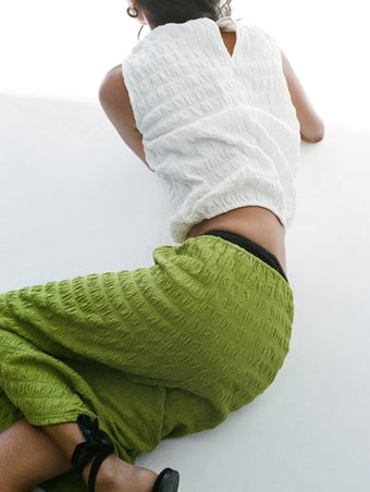 Proenza Schouler Editorial Cropped Image of model laying on white floor wearing the Lori Skirt in Textured Cotton in Apple with the Bradley Crewneck in Textured Cotton in White