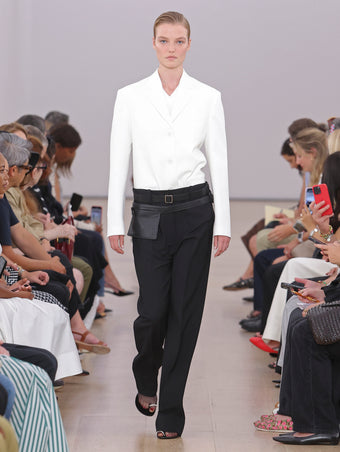 Model Walking Proenza Schouler SS24 Runway In Talia T-shirt In White Eco Cotton Jersey, Otis Pant In Black Viscose Wool Suiting, Sandis Jacket In White Cotton Viscose Suiting, Zip Belt Bag In Black Calf Leather, Tee Toe Ring Sandals In Black + Cream Nappa Lux