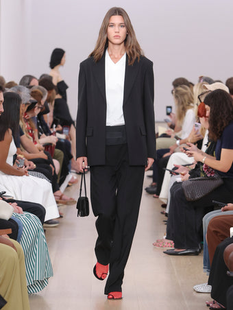 Model Walking Proenza Schouler SS24 Runway In Talia T-shirt In White Cotton Mesh, Otis Pant In Black Viscose Wool Suiting, Devon Jacket In Viscose Wool Suiting, Flip Shoulder Bag In Black Silk Satin, Tee Toe Ring Sandals In Black + Red Nappa Lux