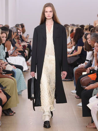 Model Walking Proenza Schouler SS24 Runway In Tauba Dress In Resin Satin Ribbon, Roy Jean In Ecru Lacquered Leather, Silva Coat In Black Viscose Wool Suiting, City Messenger Bag In Black Nappa Leather, Bronco Chelsea Boots In Black Shiny Calf