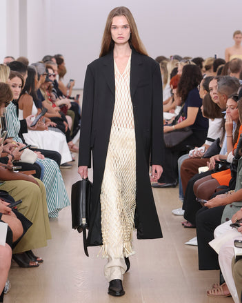 Model Walking Proenza Schouler SS24 Runway In Tauba Dress In Resin Satin Ribbon, Roy Jean In Ecru Lacquered Leather, Silva Coat In Black Viscose Wool Suiting, City Messenger Bag In Black Nappa Leather, Bronco Chelsea Boots In Black Shiny Calf