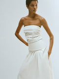 Cropped editorial image of model standing in front of blank white wall wearing the Maisy Strapless Top in Poplin in White with the Nessa Skirt in Poplin in White