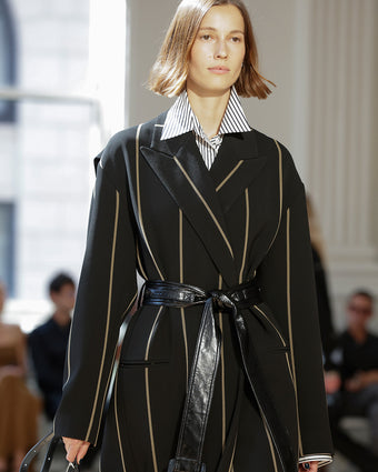 4x5 Image of model in Look 10 from SS25, a black coat with tan stripes a leather belt over a striped button down shirt