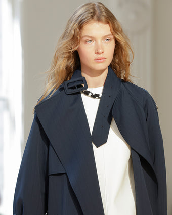 4x5 Image of model in Look 18 from SS25, wearing a navy coat over a white leather top and black and white necklace 