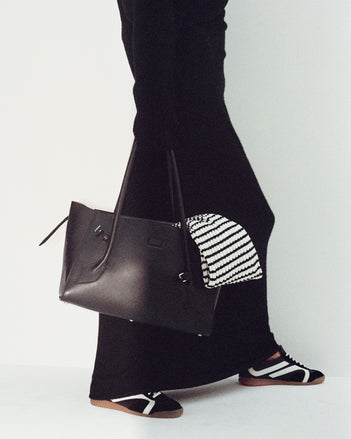 Cropped image of model wearing Annette Dress in Cashmere Silk in black with Track Sneakers in black/white, carrying Tate Bag in black