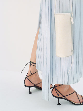 Cropped image of model wearing Hannah Dress in Stripe Silk Twill in pale blue multi with Tee Ankle Strap Sandals in black, carrying Silo Bag in cream