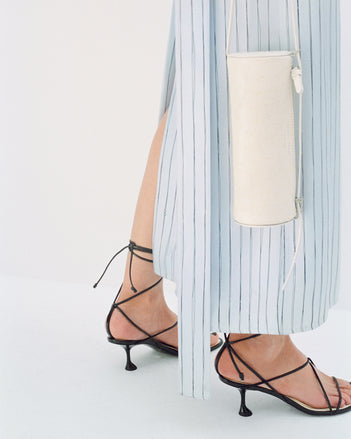Cropped image of model wearing Hannah Dress in Stripe Silk Twill in pale blue multi with Tee Ankle Strap Sandals in black, carrying Silo Bag in cream