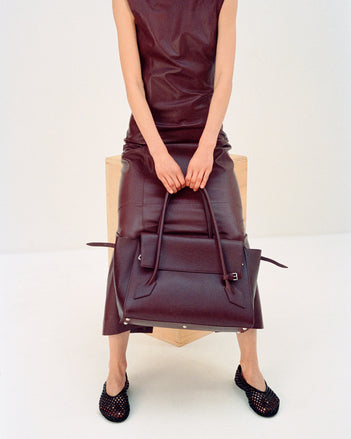 Cropped image of model wearing Backless Leather Dress in Ox Blood with Tee Perforated Ballerina Flats in black, carrying Tate Bag in dark red 