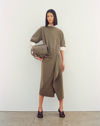 Image of model wearing Maisie Dress in Matte Double Crepe in wood with Tee Perforated Slingback Pumps in black, carrying Tate Bag in Nubuck Calf in slate