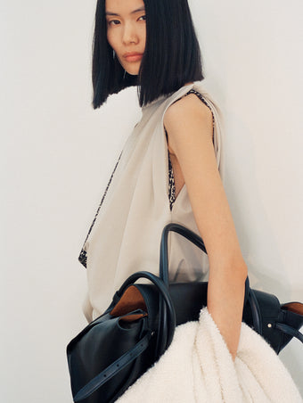 Cropped image of model wearing Elena Dress in Wool Gabardine Suiting in taupe carrying Tate Bag in black