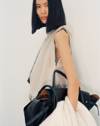Cropped image of model wearing Elena Dress in Wool Gabardine Suiting in taupe carrying Tate Bag in black