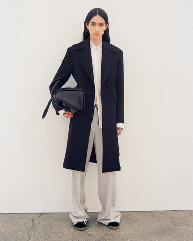 Image of model wearing Thea Coat in Wool Gabardine Suiting in black and Savannah Pant in Wool Gabardine Suiting in taupe with Track Sneakers in black/white, carrying Tate Bag in black