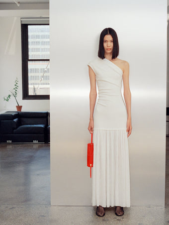 Image of model wearing Cora Dress in Pleated Crepe Chiffon in ivory with Tee Perforated Slingback Pumps in black, carrying Silo Bag in red