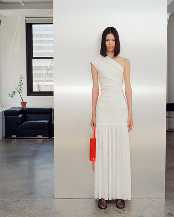 Image of model wearing Cora Dress in Pleated Crepe Chiffon in ivory with Tee Perforated Slingback Pumps in black, carrying Silo Bag in red