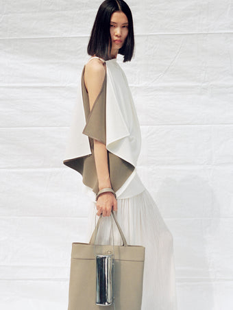 Cropped image of model wearing Alyssa Top in Matte Double Crepe and Paige Skirt in Pleated Crepe Chiffon in ivory, carrying Split Tote in beige and Silo Bag in silver