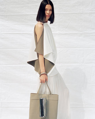 Cropped image of model wearing Alyssa Top in Matte Double Crepe and Paige Skirt in Pleated Crepe Chiffon in ivory, carrying Split Tote in beige and Silo Bag in silver