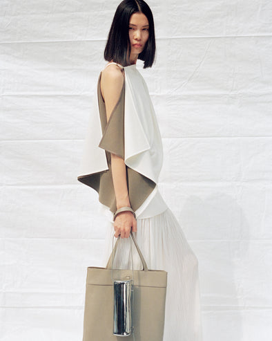 Cropped image of model wearing Alyssa Top in Matte Double Crepe and Paige Skirt in Pleated Crepe Chiffon in ivory, carrying Split Tote in beige and Silo Bag in silver
