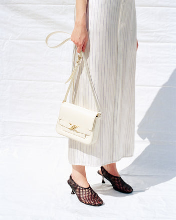 Cropped image of model wearing Hannah Dress in Stripe Silk Twill in ivory multi with Tee Perforated Slingback Pumps in black, carrying Box Bag in cream
