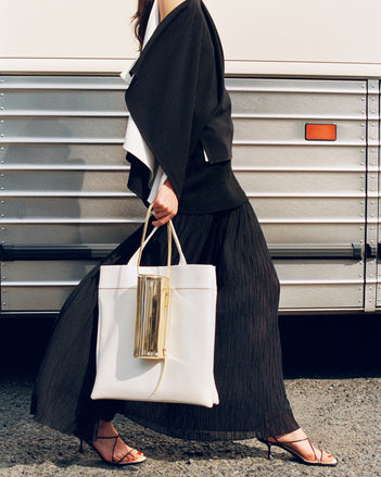 Cropped image of model wearing Alyssa Top in Matte Double Crepe and Paige Skirt in Pleated Crepe Chiffon in black, carrying Split Tote in cream and Silo Bag in gold