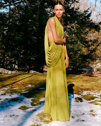 Model standing in snowy field of moss wearing Bari Dress in Olive Gauzy Jersey and Uma Ankle Boots in Paper Slick Calf