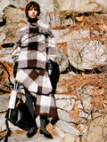 Model standing against wall of rock and foliage wearing Kai Top in Brown Brushed Glenplaid Knit, Kai Skirt Brown Brushed Glenplaid Knit, Days Carryall in Black Paper Calf, Silo Bag in Light Grey Croc Embossed Calf, and Slash Flats in Black Spazzolato