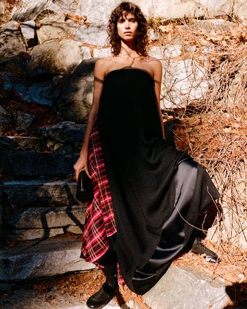 Model standing against stone staircase and wall wearing Elea Dress in Rust Boucle Plaid Suiting, Silo Clutch in Black Shiny Calf, and Arcadia Sneakers in Black Calfsuede