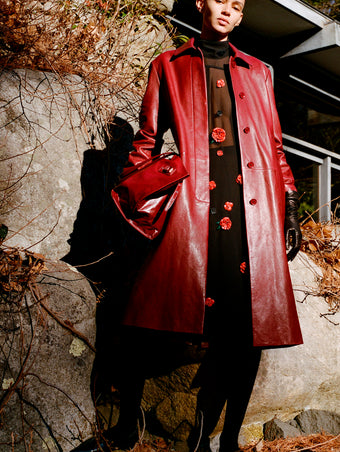 Proenza Schouler Front full length image of model wearing Nissi Coat In Semigloss Leather in Burgundy standing against rocks. 