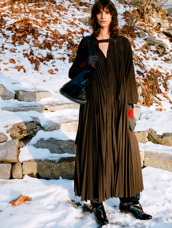 Model standing on snowy stone steps wearing Fanni Dress in Espresso Wool Jersey, Argyle Gloves in Grey Cashmere, Days Carryall in Black Paper Calf, and Uma Over the Knee Boots in Black Slick Calf