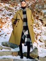 Model standing on snowy stone steps wearing Adelaide Coat in Moss Cotton Viscose, Kai Top in Black Brushed Glenplaid Knit, Kai Skirt in Black Brushed Glenplaid Knit, Crossbody Silo in Cedar Shiny Calf, and Slash Flats in Black Spazzolato