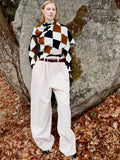 Model standing against stone boulder wearing Vanne Top in Light Green Argyle Velvet Knit, Salome Pant in Ecru Corduroy, Braid Belt in Bordeaux Croc Embossed Calf, and Uma Ankle Boots in Black Silk Calf