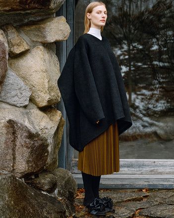 Model standing against glass back door wearing Bea Top in Black Wool Cashmere Double Face, Fox Sweater in White Viscose Rib, Eda Skirt in Tobacco Wool Jersey, and Tee Souvenir Sandals in Black Satin