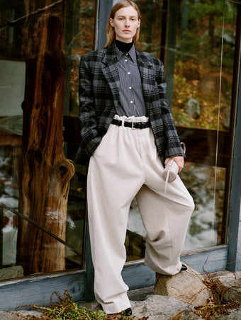 Model standing in against glass back door of wooded home wearing Daria Jacket in Grey Plaid Wool Suiting, Lynsey Top Black/White Viscose Striped Shirting, Fox Sweater in Black Viscose Rib, Salome Pant in Ecru Corduroy, Silo Bag in Light Grey Croc Embossed Calf, Braid Belt in Black Calf, and Uma Ankle Boots in Black Slick Calf