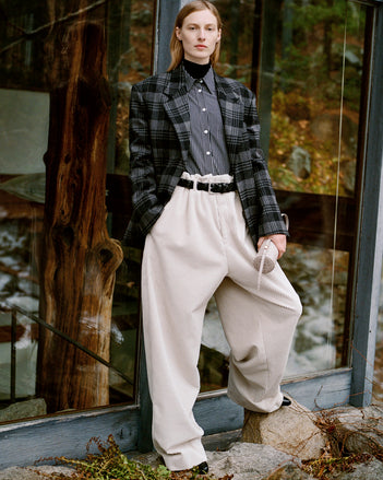 Model standing in against glass back door of wooded home wearing Daria Jacket in Grey Plaid Wool Suiting, Lynsey Top Black/White Viscose Striped Shirting, Fox Sweater in Black Viscose Rib, Salome Pant in Ecru Corduroy, Silo Bag in Light Grey Croc Embossed Calf, Braid Belt in Black Calf, and Uma Ankle Boots in Black Slick Calf