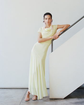 Full body image of model wearing the Tamara dress against a white wall leaning on white stairs with a silver railing 