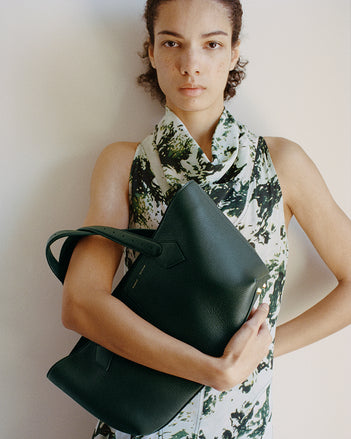 Model wearing a green printed dress and holding the East West tote 
