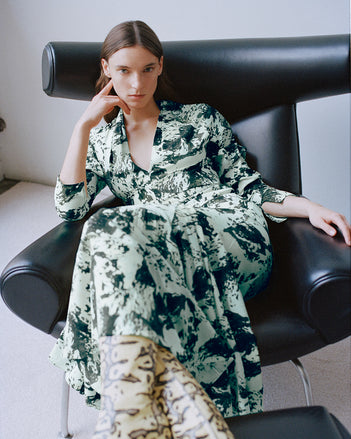 Model wearing a printed top and skirt sitting in a black sofa chair 