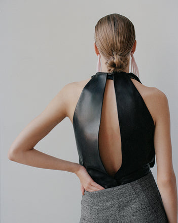 Model facing a white wall wearing black leather top with opening 
