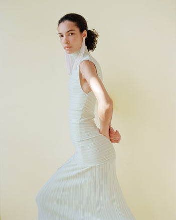 Model wearing the Federica dress against a light yellow wall with long pink earrings 