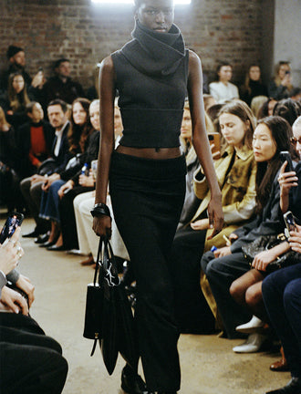Cropped image of model walking Proenza Schouler FW24 Runway wearing Cruz Vest in Midweight Viscose Rib in grey with Avalon Skirt in Lacquered Viscose in black