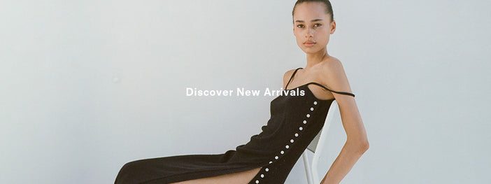 Image of model sitting in chair wearing Astrid Knit Dress in Boucle Viscose in black, 'Discover New Arrivals' overlaid